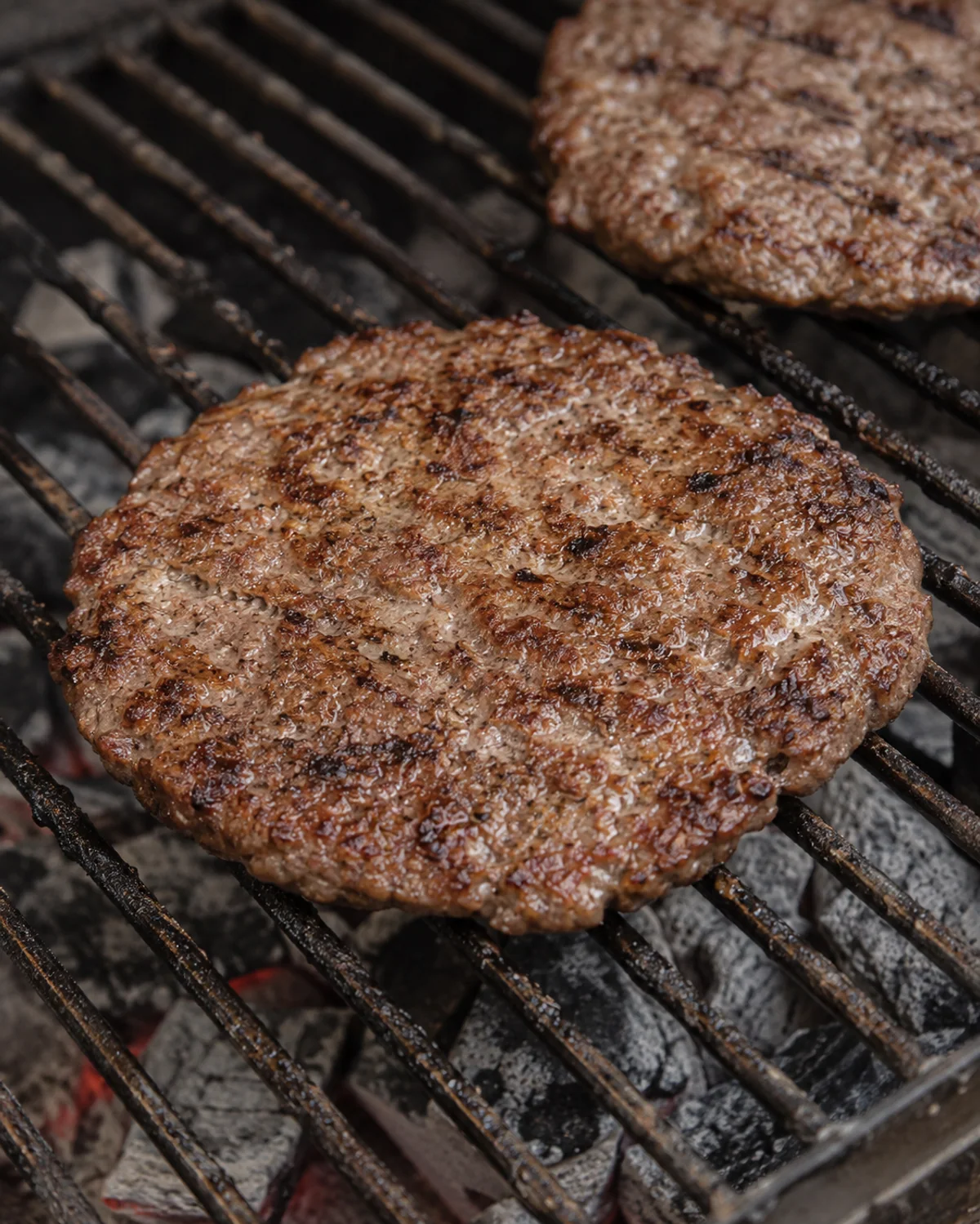 Hand-shaped pljeskavica with natural browning on a charcoal grill